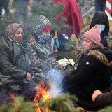 Vier Frauen sitzen in Mützen und Kopftüchern sowie warmer Kleidung um ein Lagerfeuer herum