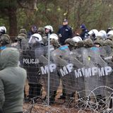 Hinter einem etwa zwei Meter hohen Drahtzaun stehen Polizisten in voller Rüstung und mit Schilden in Reih und Glied