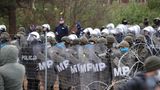 Hinter einem etwa zwei Meter hohen Drahtzaun stehen Polizisten in voller Rüstung und mit Schilden in Reih und Glied