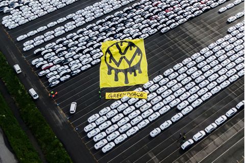 Greenpeace-Aktivisten breiten ein riesiges Protesttransparent über Autos aus.