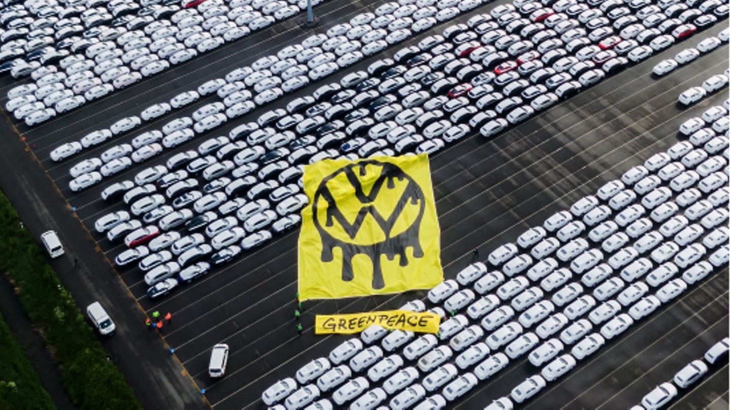 Greenpeace-Aktivisten breiten ein riesiges Protesttransparent über Autos aus.
