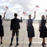 Eine Lufthansa-Crew in tradioneller Bavaria-Uniform schwingt USA-Fähnchen zum Abschied des Airbus A350.
