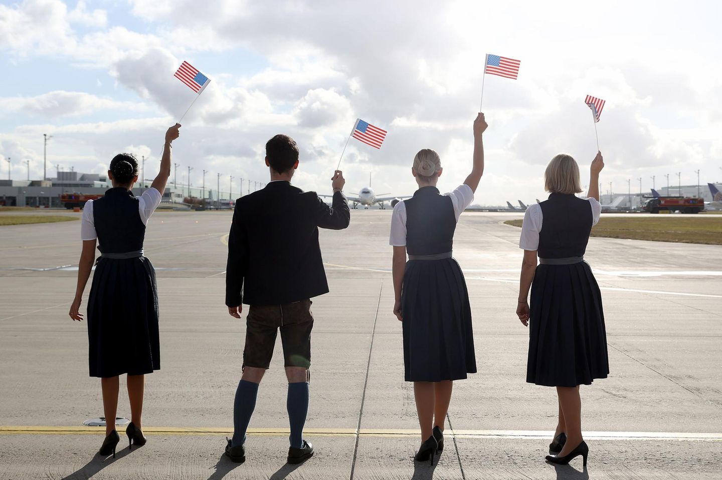 Eine Lufthansa-Crew in tradioneller Bavaria-Uniform schwingt USA-Fähnchen zum Abschied des Airbus A350.