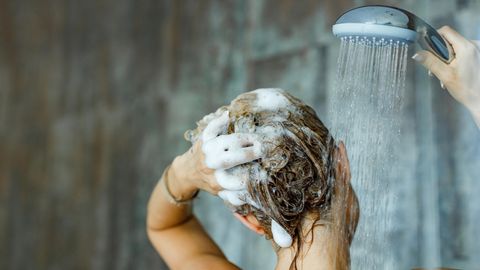 Frau mit eingeschäumten Haaren steht unter der Dusche