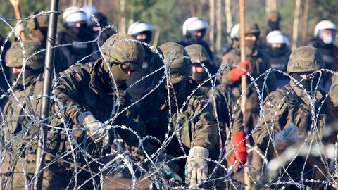 Polnische Polizisten und Grenzschützer stehen am Stacheldraht, während sich Migranten aus dem Nahen Osten und anderen Ländern auf den Weg machen.