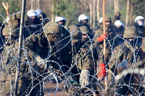Polnische Polizisten und Grenzschützer stehen am Stacheldraht, während sich Migranten aus dem Nahen Osten und anderen Ländern auf den Weg machen.