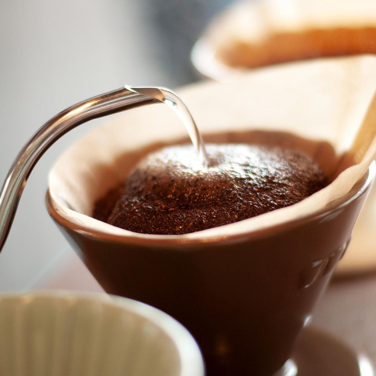 Der Aufguss  Schritt 5: Niemals den Kaffee mit kochendem Wasser übergießen!  Der von Hand aufgebrühte Kaffee schmeckt aromatischer und runder, wenn das Wasser nicht mehr kocht, wenn es mit ihm in Berührung kommt. Bei zu großer Hitze verflüchtigen sich die Aromastoffe und die bitteren und sauren Komponenten treten in den Vordergrund. Ideal ist eine Temperatur von 86 bis 89 Grad Celsius. Das Kaffeemehl nun mit einem kleinen Schwall Wasser anfeuchten und es 20 Sekunden quellen lassen. Auf diese Weise werden die gerösteten Öle, Fette und Bitterstoffe gelöst. Nun das Wasser in kleinen Mengen alle zehn Sekunden schwallweise nachgießen. Der Vorgang sollte vier bis sechs Minuten dauern. Unter vier Minuten entfalten sich die Aromen nicht, über sechs Minuten verflüchtigen sie sich bereits. Das manuelle Aufbrühen ist auch heute noch die Methode, mit der Kaffeetester die Qualität der Ware beurteilen.