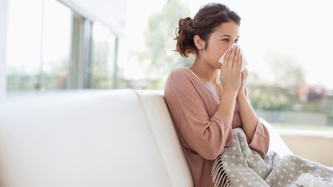 Erkältete Frau sitzt auf einem Sofa und putzt sich die Nase