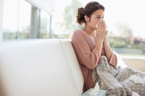 Erkältete Frau sitzt auf einem Sofa und putzt sich die Nase