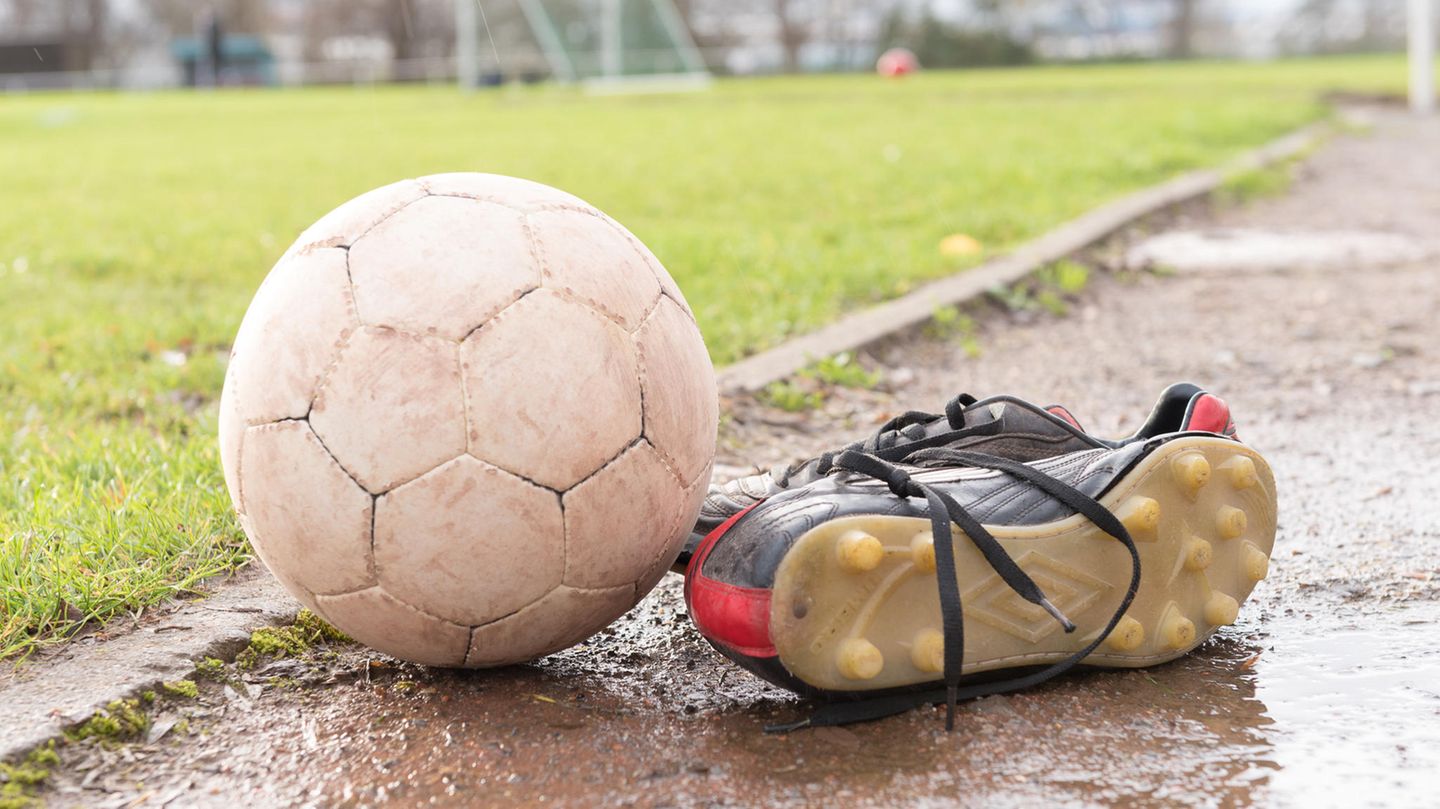 Ein Fußball und Fußballschuhe liegen am Rand eines Sportplatzes