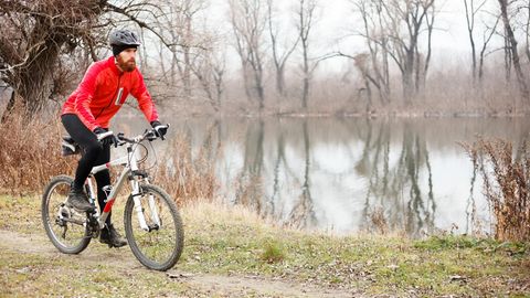 Radmode für Männer: Mann fährt auf einem Mountainbike an einem See entlang