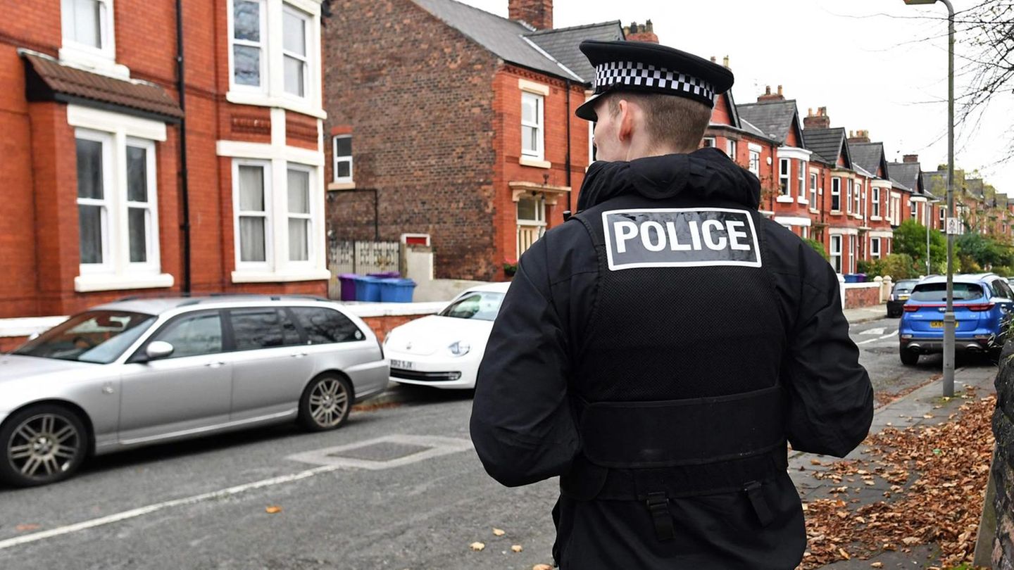 Hinter blau-weißem Absperrband steht ein englischer Polizist in Uniform und kehrt dem Fotografen den Rücken zu