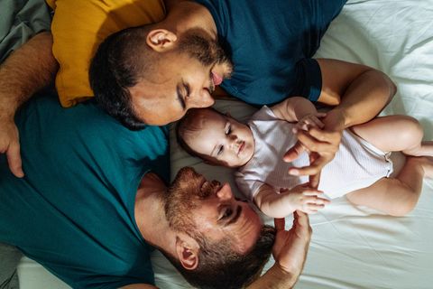 Homosexuelles Paar genießt im Bett liegend die Zeit mit adoptiertem Baby