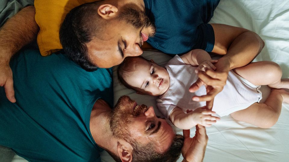 Homosexuelles Paar genießt im Bett liegend die Zeit mit adoptiertem Baby