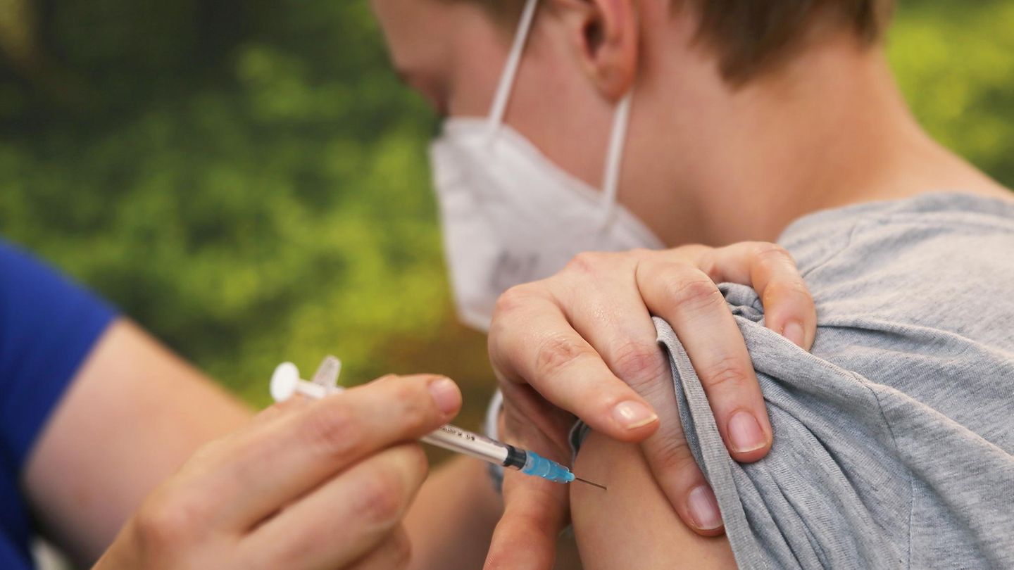 Corona Impfung Jugendliche Kinder Eine linke Hand drückt den Oberarmmuskel eines Jungen zusammen, während eine rechte Hand eine Spritze hält