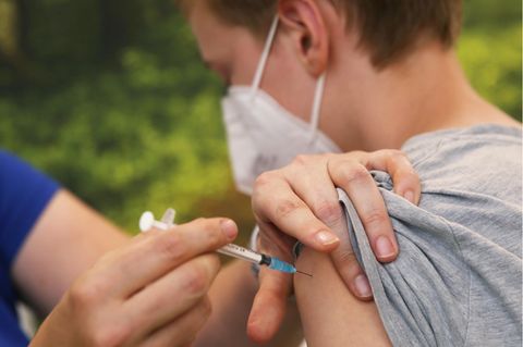 Eine linke Hand drückt den Oberarmmuskel eines Jungen zusammen, während eine rechte Hand eine Spritze hält