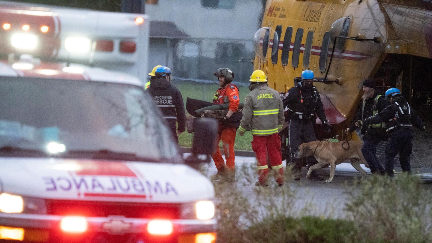 Rettungskräfte helfen Flutopfern beim Aussteigen aus einem Hubschrauber, während ein Krankenwagen abfährt