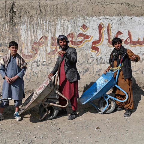 Zwei Männer und ein Jugendlicher in traditioneller afghanischer Kleidung stehen mit Schubkarren Schlange für Essen