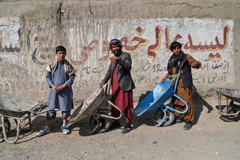 Zwei Männer und ein Jugendlicher in traditioneller afghanischer Kleidung stehen mit Schubkarren Schlange für Essen