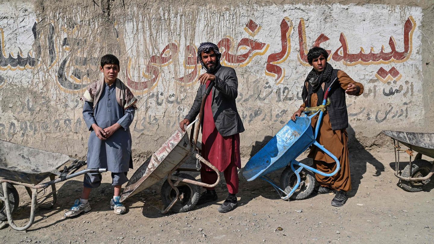 Zwei Männer und ein Jugendlicher in traditioneller afghanischer Kleidung stehen mit Schubkarren Schlange für Essen