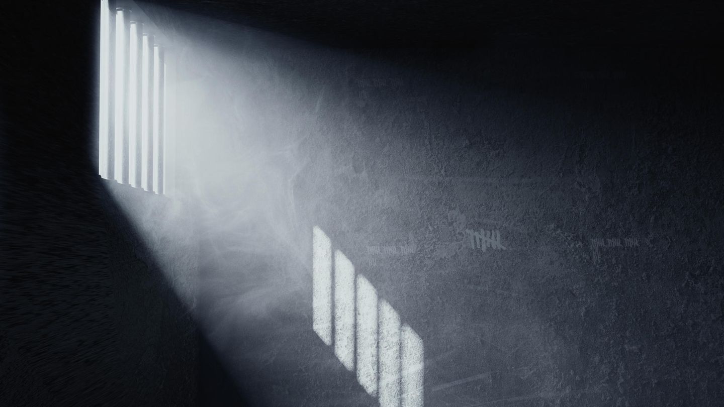 Licht fällt durch Gitterstäbe einer Gefängniszelle auf die Wand