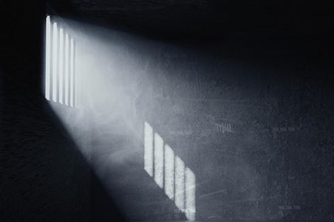 Licht fällt durch Gitterstäbe einer Gefängniszelle auf die Wand