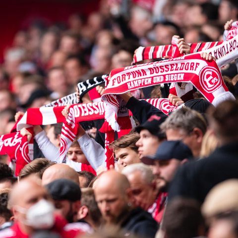 Aus einer Menschenmasse in einem Stadion recken Arme rot-weiße Fanschals von Fortuna Düsseldorf hoch