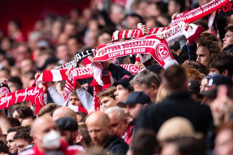 Aus einer Menschenmasse in einem Stadion recken Arme rot-weiße Fanschals von Fortuna Düsseldorf hoch
