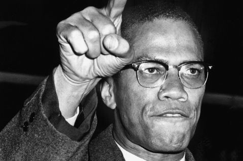 Malcolm X blickt entschlossen und recht eine Hand in die Höhe