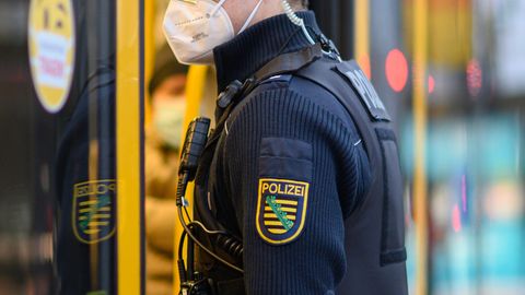Ein weißer Mann in dunkelblauer Polizeiuniform und Wappen von Sachsen auf dem Arm steht an der Tür einer gelben Straßenbahn