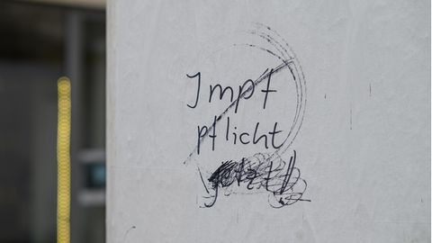 Eine leere Litfaßsäule ist mit dem durchgestrichenen Schriftzug "Impfpflicht jetzt!" beschmiert