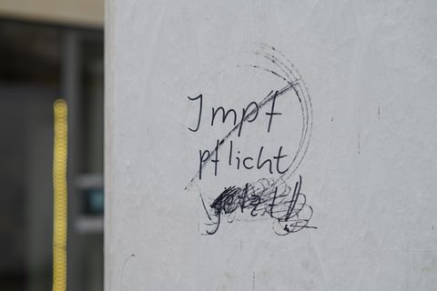 Eine leere Litfaßsäule ist mit dem durchgestrichenen Schriftzug "Impfpflicht jetzt!" beschmiert