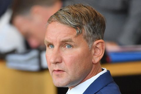 Ein weißer Mann mit angegrautem Seitenscheitel sitzt in blauem Jackett und weißem Hemd in einem Plenarsaal