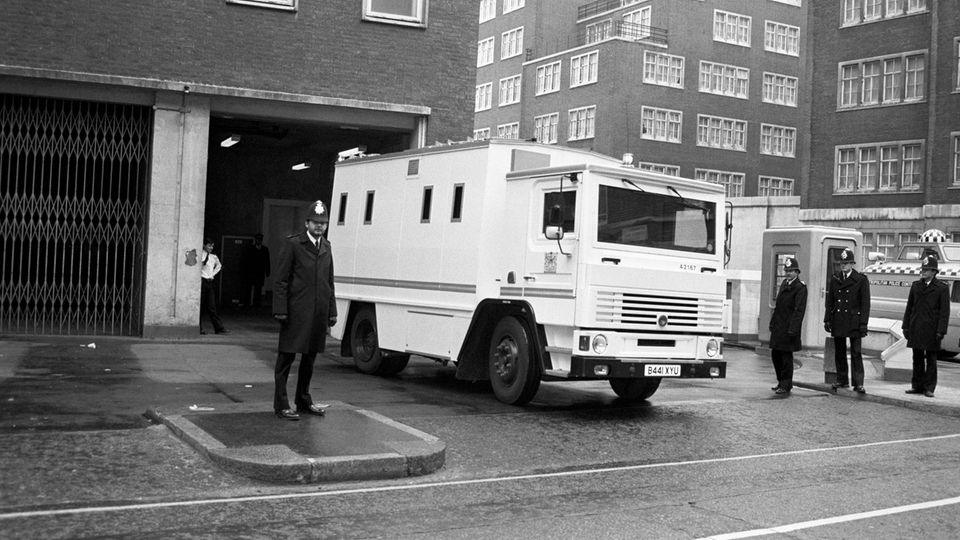 Ein weißer Transporter auf eine Schwarzweiß-Foto, im Vordergrund ist ein englischer Polizist zu sehen
