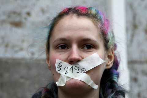 Eine junge weiße Frau mit bunt gefärbten Haaren hat sich mit weißem Tape den Mund zugeklebt