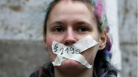 Eine junge weiße Frau mit bunt gefärbten Haaren hat sich mit weißem Tape den Mund zugeklebt