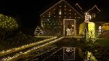 usgesägte Krippenfiguren, mit Lichtern umrahmt, leuchten im Garten eines sogenannten Weihnachtshauses