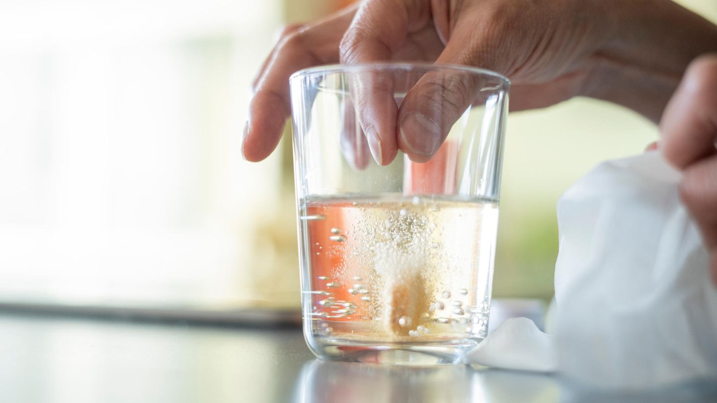 Eine Hand lässt eine Tablette in ein Wasserglas fallen