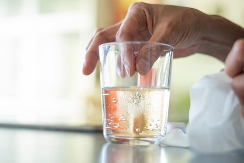 Eine Hand lässt eine Tablette in ein Wasserglas fallen