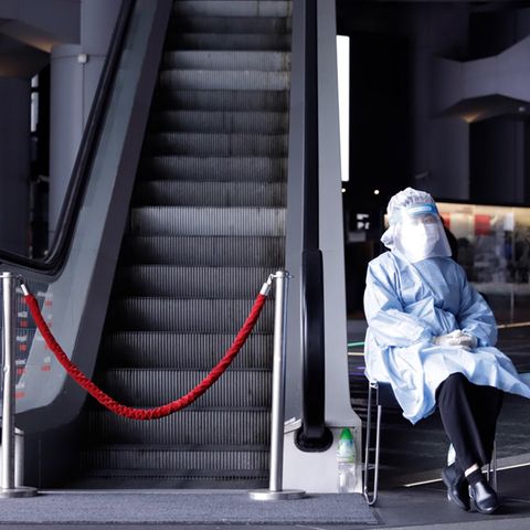 China, Hongkong: Eine Pflegemitarbeiterin in Schutzkleidung sitzt neben einer Rolltreppe