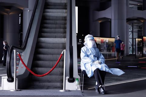 China, Hongkong: Eine Pflegemitarbeiterin in Schutzkleidung sitzt neben einer Rolltreppe