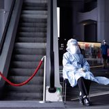 China, Hongkong: Eine Pflegemitarbeiterin in Schutzkleidung sitzt neben einer Rolltreppe