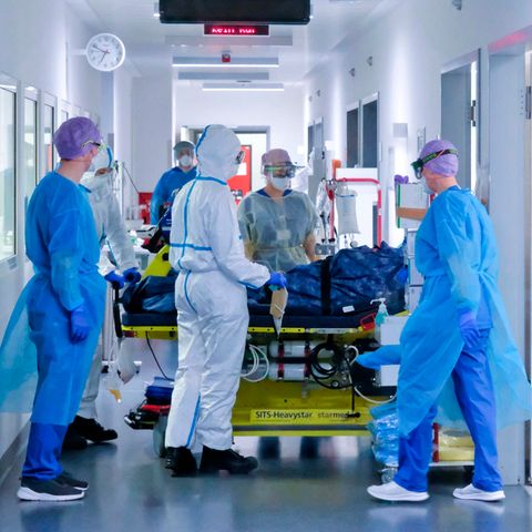 Mehrere Menschen in voller medizinischer Schutzkleidung kümmern sich um einen beatmeten Patienten auf einer Liege