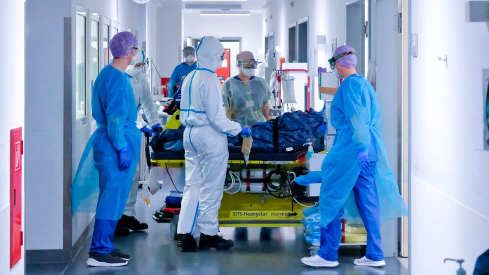 Mehrere Menschen in voller medizinischer Schutzkleidung kümmern sich um einen beatmeten Patienten auf einer Liege