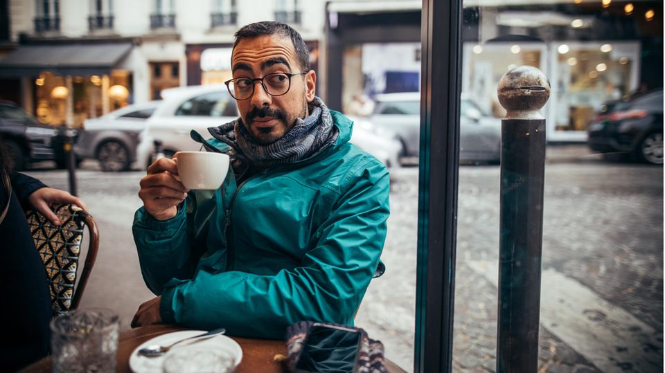 Mann sitzt mit einer Tasse Kaffe in der Hand in einem Straßencafé in Frankreich