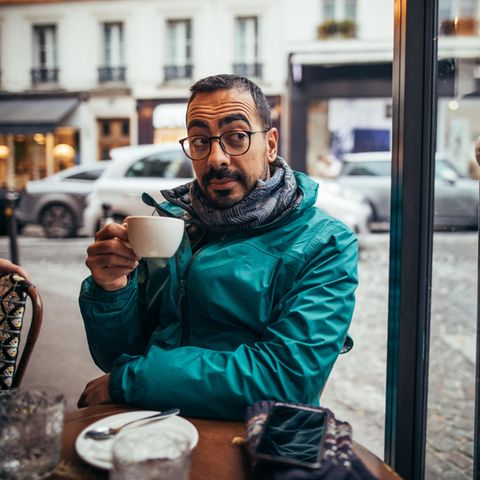 Mann sitzt mit einer Tasse Kaffe in der Hand in einem Straßencafé in Frankreich