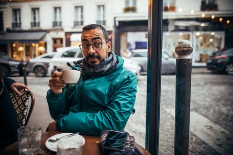 Mann sitzt mit einer Tasse Kaffe in der Hand in einem Straßencafé in Frankreich