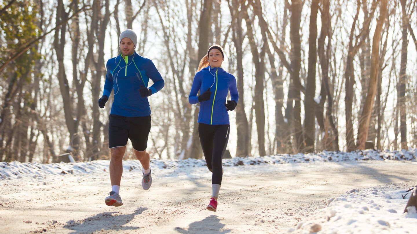 Jogging-Outfit im Winter: Pärchen läuft nebeneinander auf einem verschneiten Waldweg