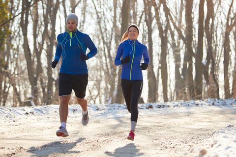 Jogging-Outfit im Winter: Pärchen läuft nebeneinander auf einem verschneiten Waldweg