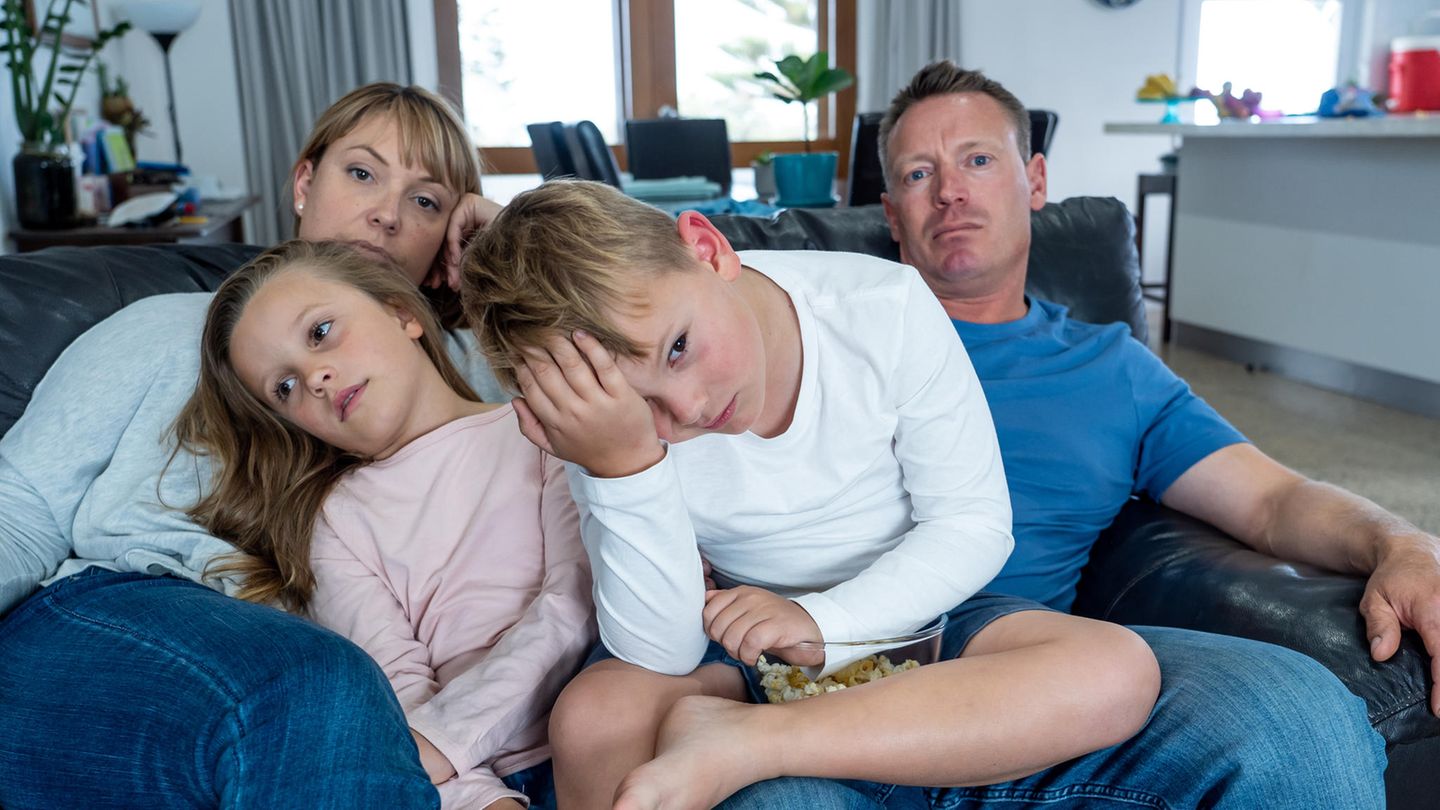 A bored family of four is sitting on a black leather sofa.  Girl and boy sitting on their parents